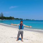 Person in straw hat walks on sunny beach with birds flying overhead