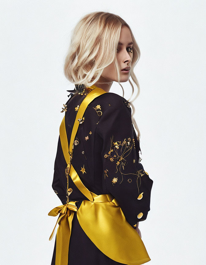 Woman in Black and Yellow Robe with Gold Patterns poses with her back to camera