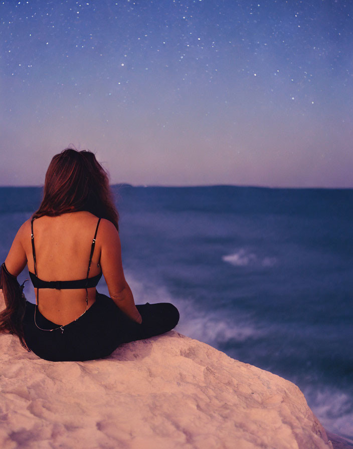 Person with Long Hair Sitting on Cliff Overlooking Sea at Night