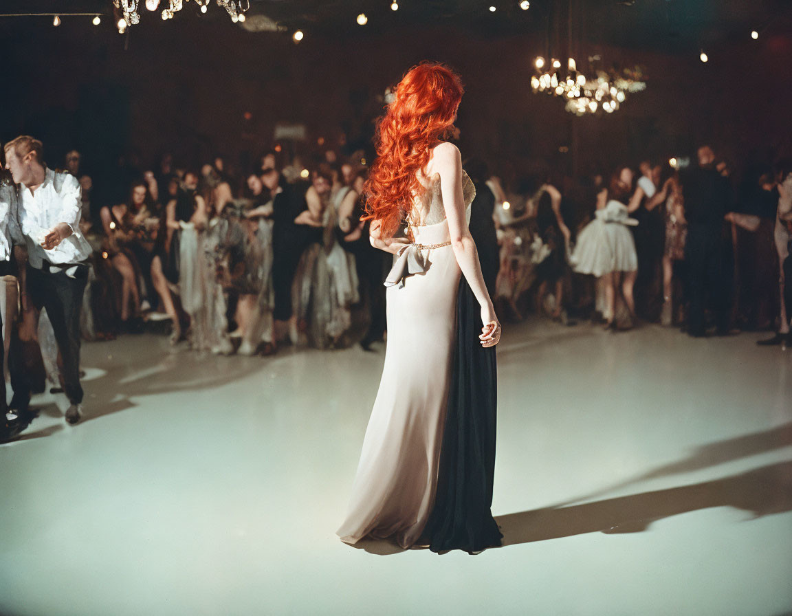 Red-haired woman in white and black gown at elegant ballroom event with dancing couples.