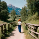 Person in Blue Skirt Walking on Rural Path with Wooden Fences and Green Fields