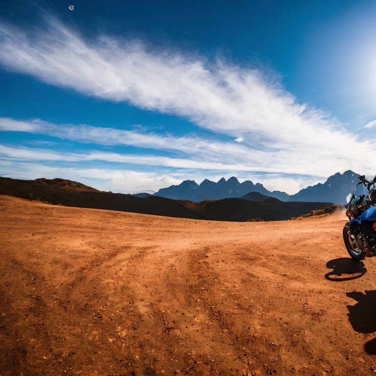 Motorcycle parked on dusty trail with mountains and blue sky