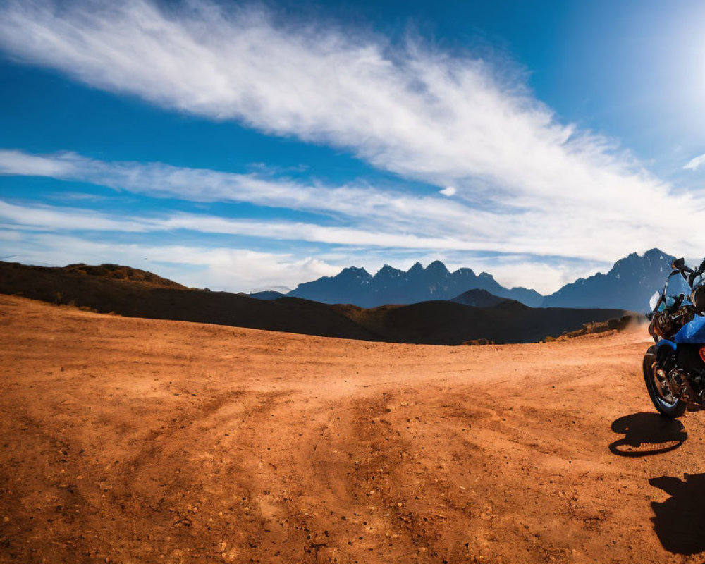 Motorcycle parked on dusty trail with mountains and blue sky