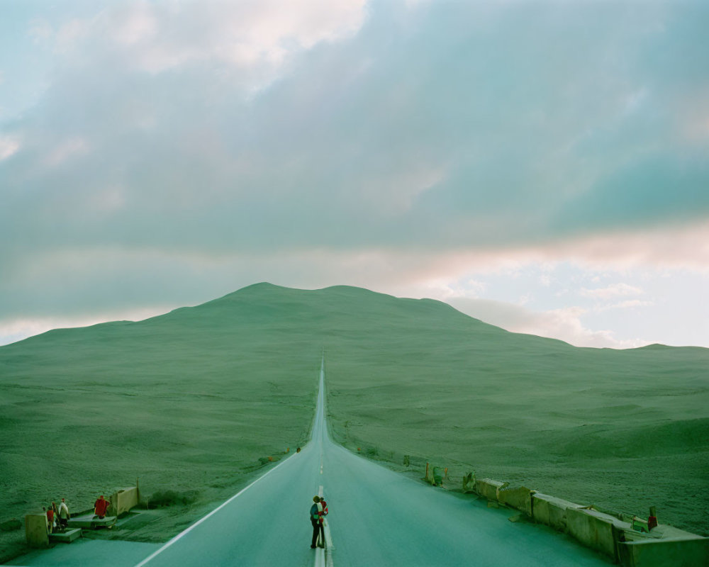 Person standing on long straight road in hilly desert landscape