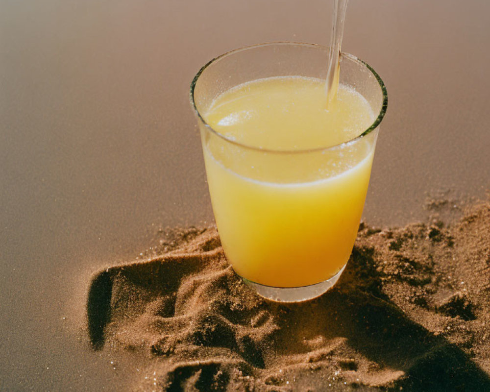 Orange Juice Glass with Straw on Sandy Beach - Refreshing Summer Beverage Concept