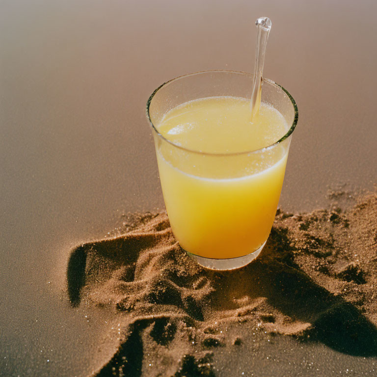 Orange Juice Glass with Straw on Sandy Beach - Refreshing Summer Beverage Concept