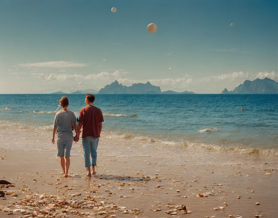 Couple walking on sandy beach with blue sky and mountain range