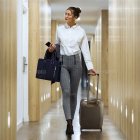 Fashionable woman in white blazer and metallic pants walking through corridor with golden orbs and vertical lights