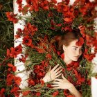 Woman reclining in bath surrounded by vibrant red roses and sunlight filtering through foliage