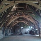 Sunlight beams through dusty air in wooden-beam barn, illuminating silhouetted figures.