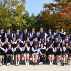 Schoolchildren with backpacks posing under autumn tree.