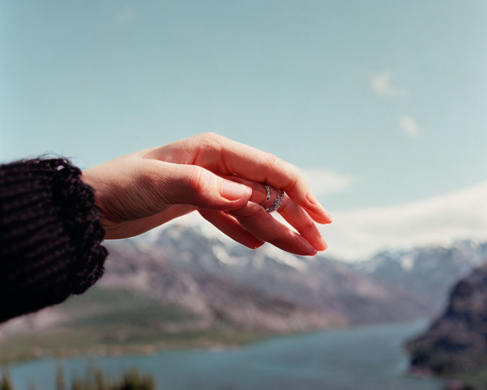 Hand with Ring Gesturing Against Lake and Mountain Backdrop