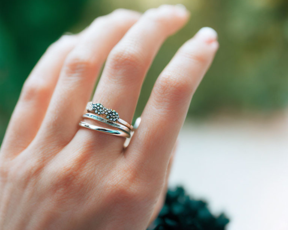 Close-up of hand with stacked rings: silver band & turquoise gemstone on blurred green background