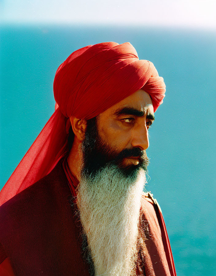 Elderly man with white beard in red turban and shawl on blue background