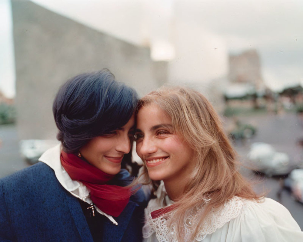 Two women with blue hair and wavy hair smiling in urban setting