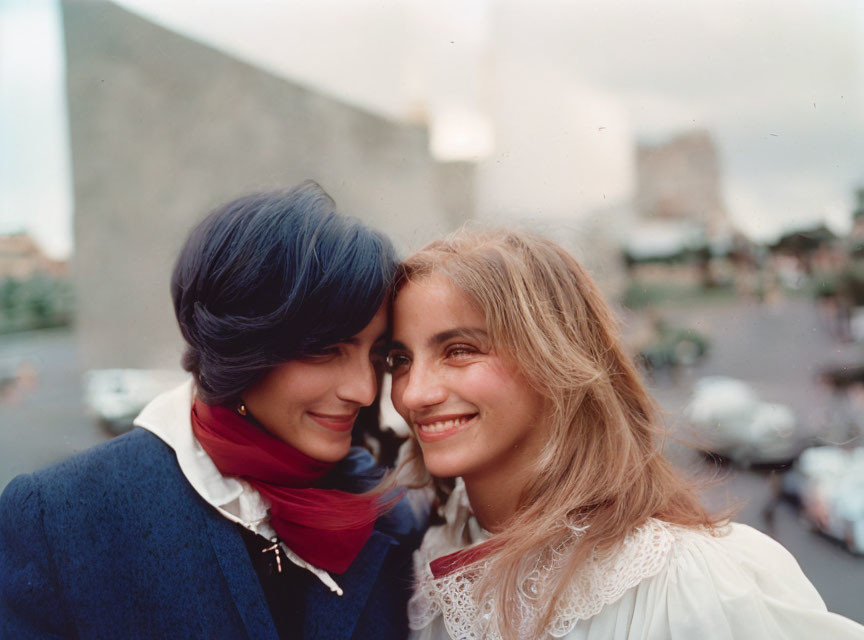 Two women with blue hair and wavy hair smiling in urban setting