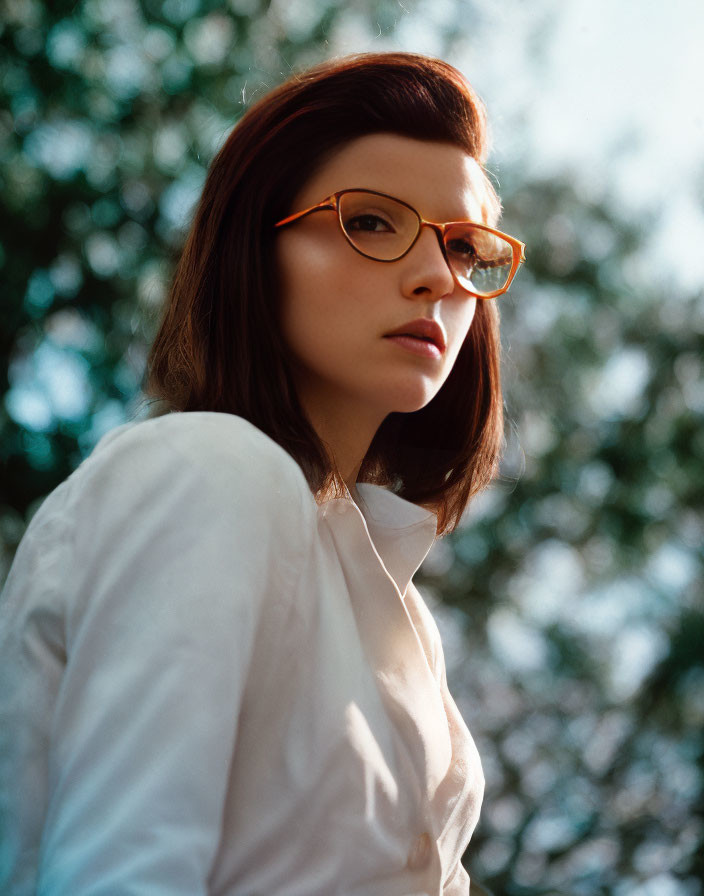 Serious woman in white shirt with orange glasses posing outdoors