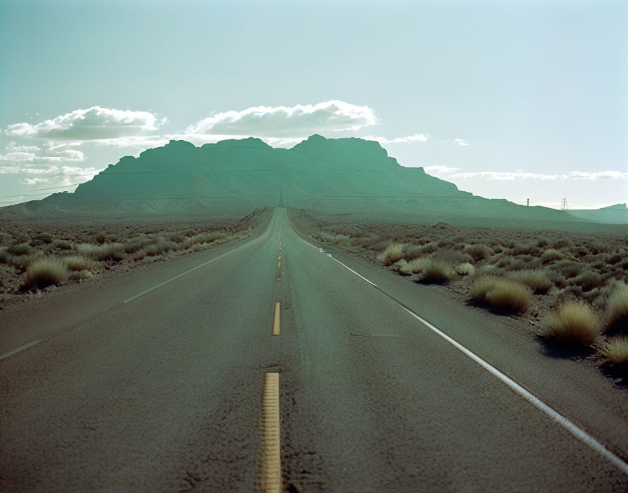 Straight road to large mountain with shrubbery under blue sky