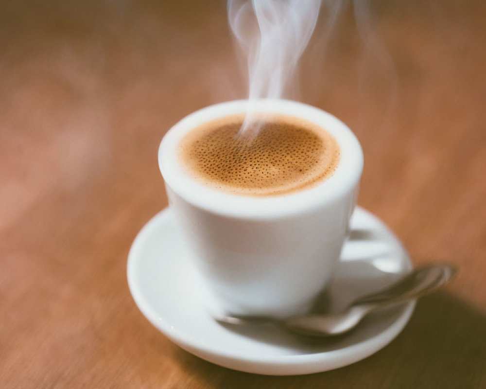 Steaming cup of coffee on wooden surface with saucer and spoon