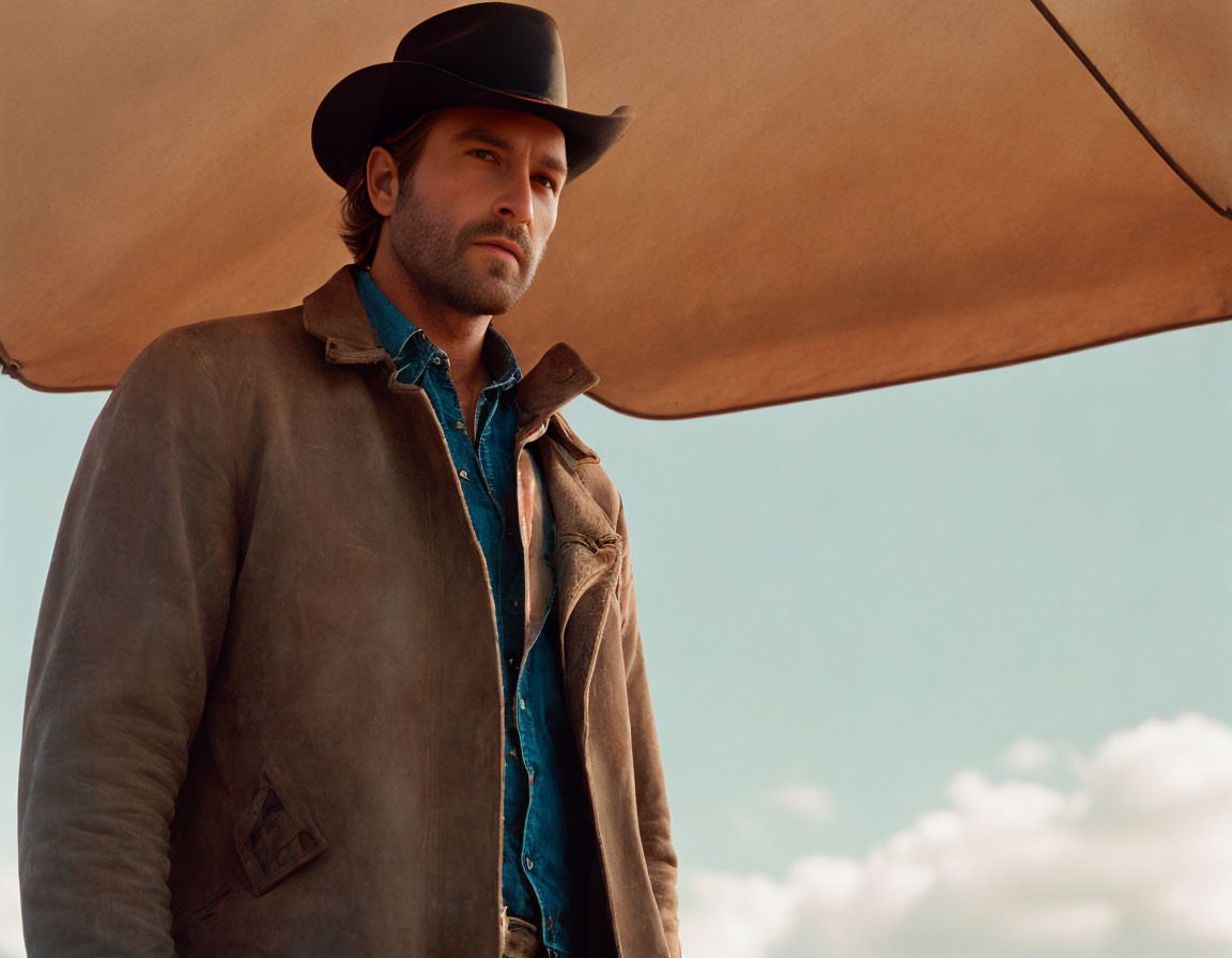 Man in Cowboy Hat and Rugged Jacket Under Wide Sky