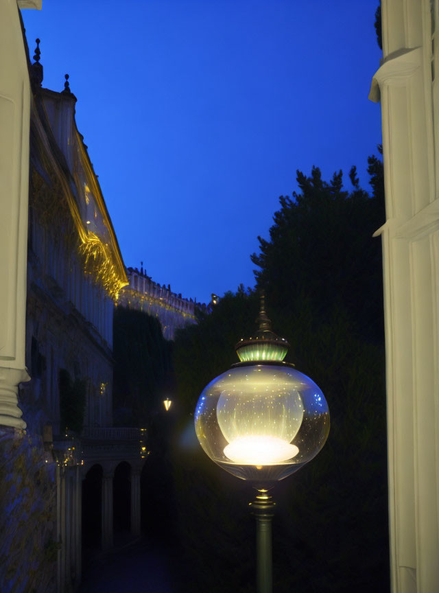 Street lamp with glass cover against twilight sky and building with lit edges