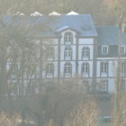 Snow-covered Victorian mansion in frosty landscape with bare trees, streetlamps, and full moon.