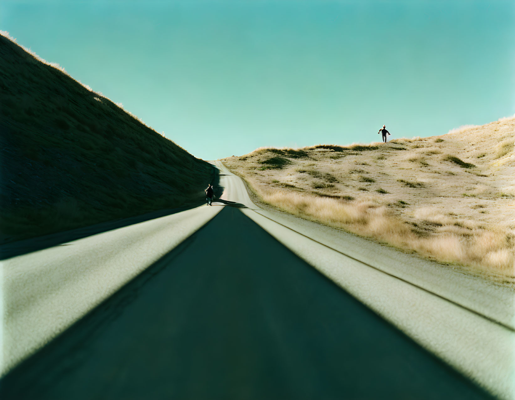 Paved road through hills with motorcycle and person under clear sky