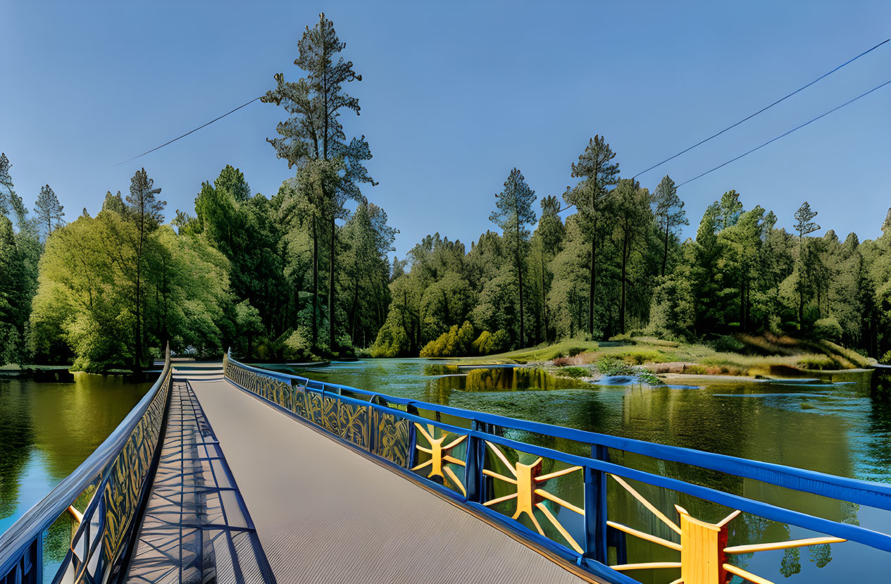 Blue footbridge over tranquil river with ornate railings and lush green trees.