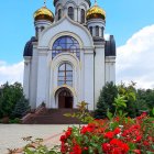 Orthodox church with golden domes, people, waterfront, and red flowers.