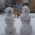 Two Large Snowmen in Winter Landscape with Building and Small Snowman at Evening