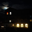 Silhouetted house against full moon with glowing windows