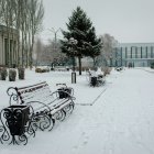 Snow-covered urban park with benches, bare trees, Christmas lights, and lone walker