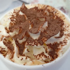 Creamy frothy beverage in white cup with chocolate powder and droplets