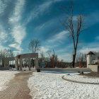 Modern park with unique arch structures, paved walkways, bare trees, and blue sky in panoramic view