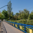 Blue footbridge over tranquil river with ornate railings and lush green trees.