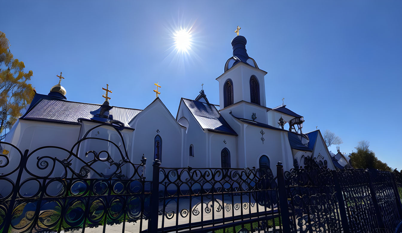 White Church with Blue Roofs under Clear Blue Sky and Sun Starburst