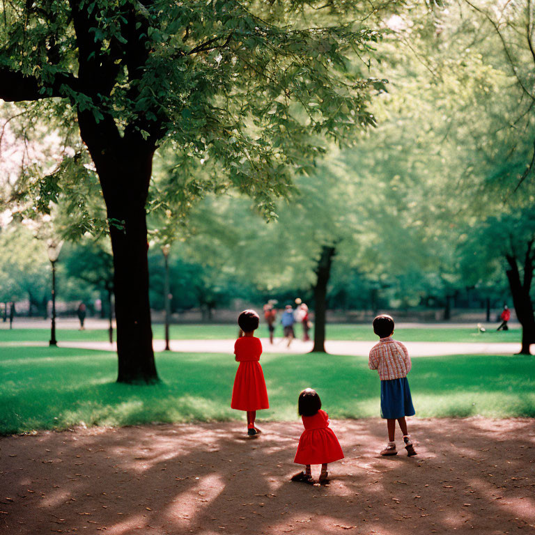 Three children in colorful clothing under trees in sunlit park.