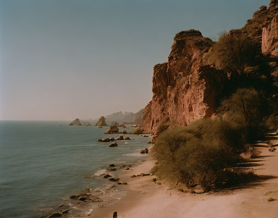 Tranquil coastal scene with rocky cliffs, calm sea, and clear sky