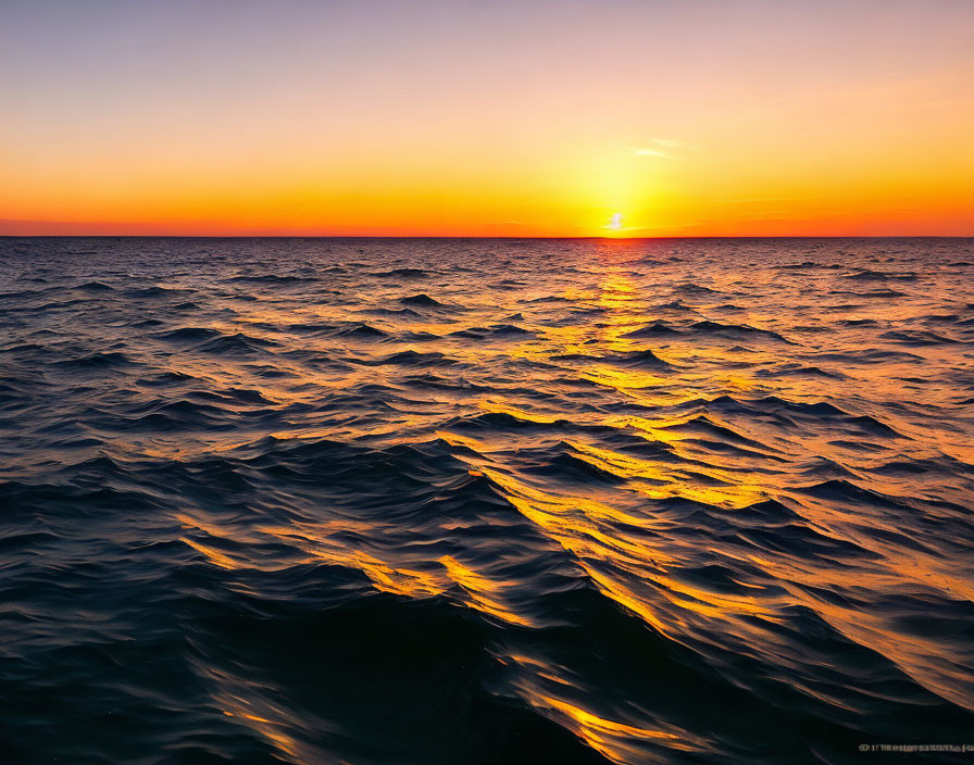 Scenic sunset over wavy sea with half-dipped sun casting orange and yellow hues