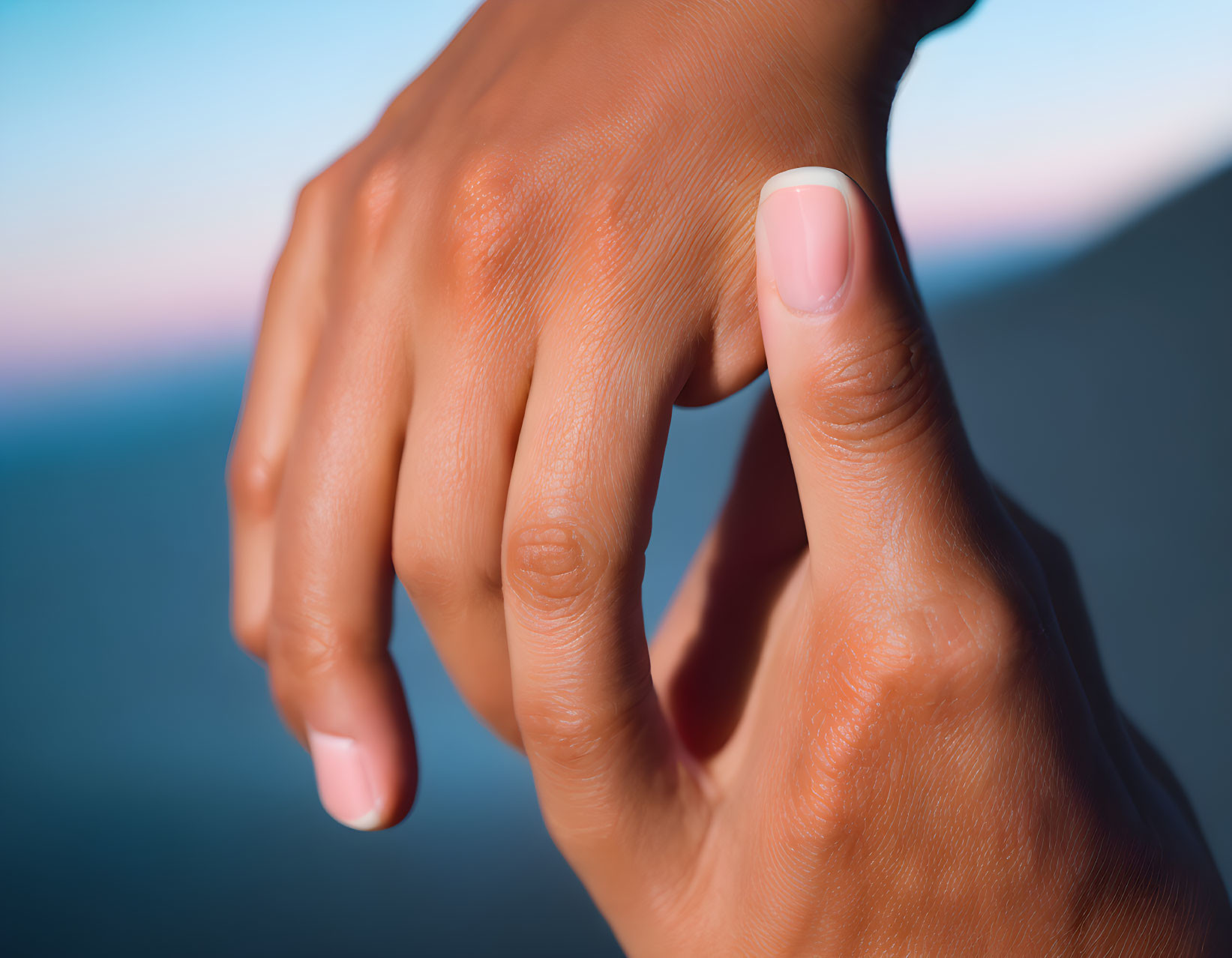 Person's Hand with Well-Manicured Nails Against Blurred Blue Background