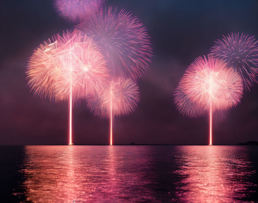 Colorful fireworks reflecting on calm water under a night sky