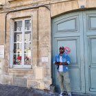 Man playing saxophone outside weathered building with blue doors.