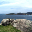 Surreal landscape with architectural structures, boats on blue sea, and bubble-like hills