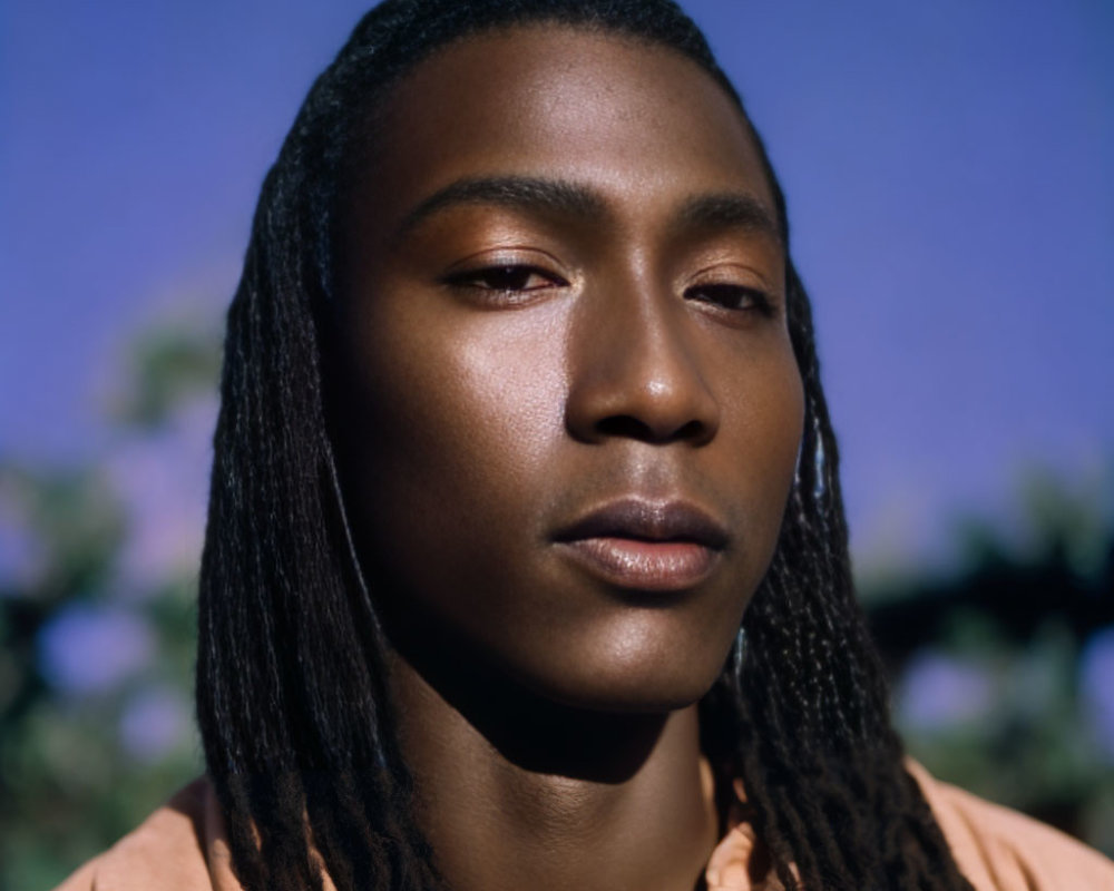 Portrait of person with braided hair gazing against blurred natural backdrop