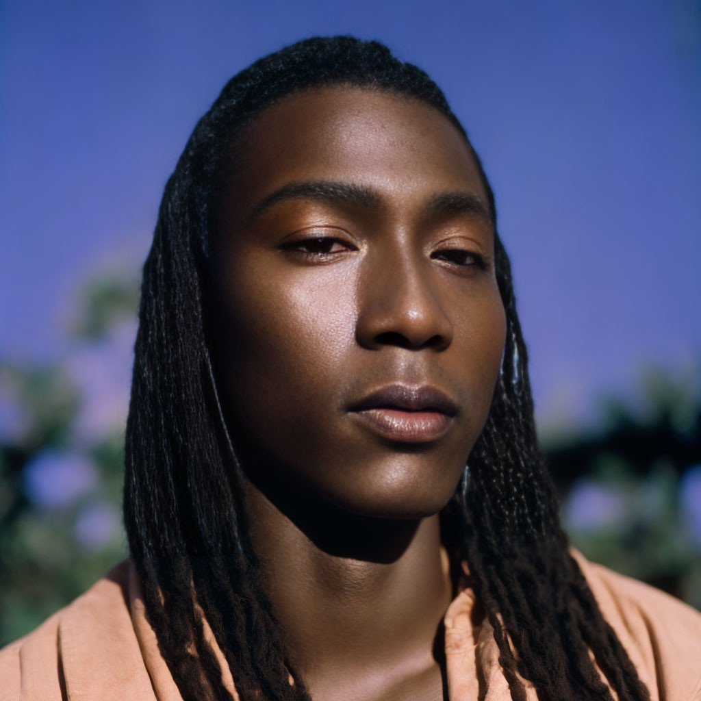 Portrait of person with braided hair gazing against blurred natural backdrop