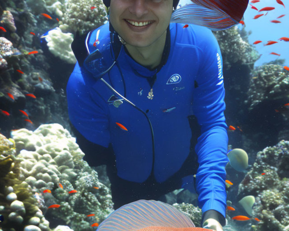 Smiling diver in blue wetsuit surrounded by fish and coral reefs