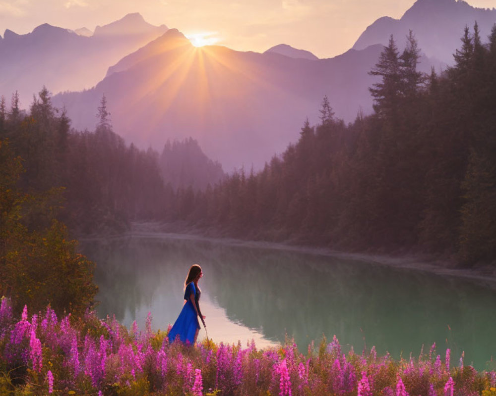 Woman in Blue Dress Standing by Lake with Purple Flowers and Sunlit Mountains