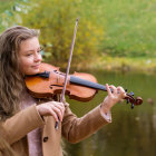 Blonde woman in white dress plays violin in sunlit field