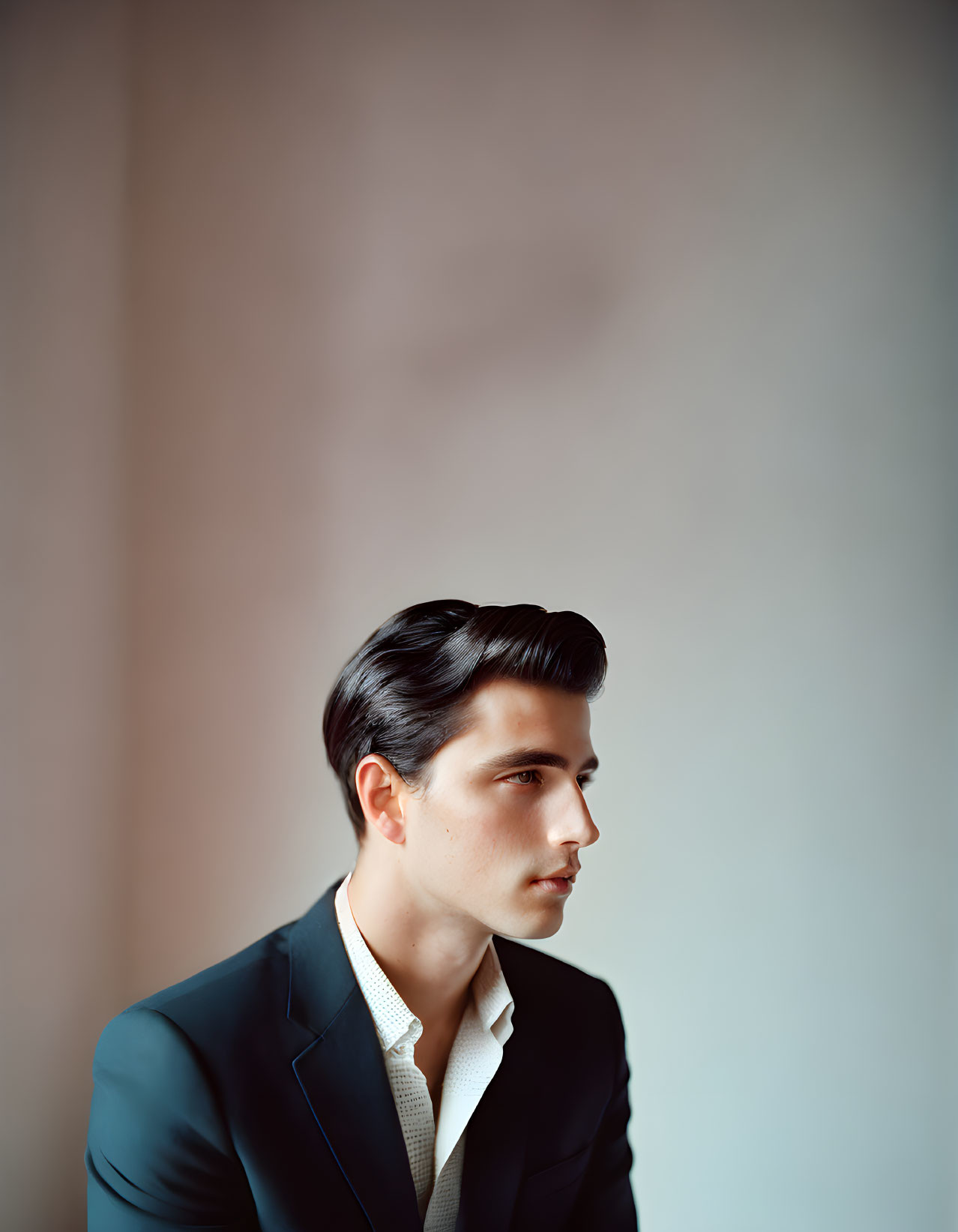 Man in Dark Suit with Slicked-Back Hair on Light Background