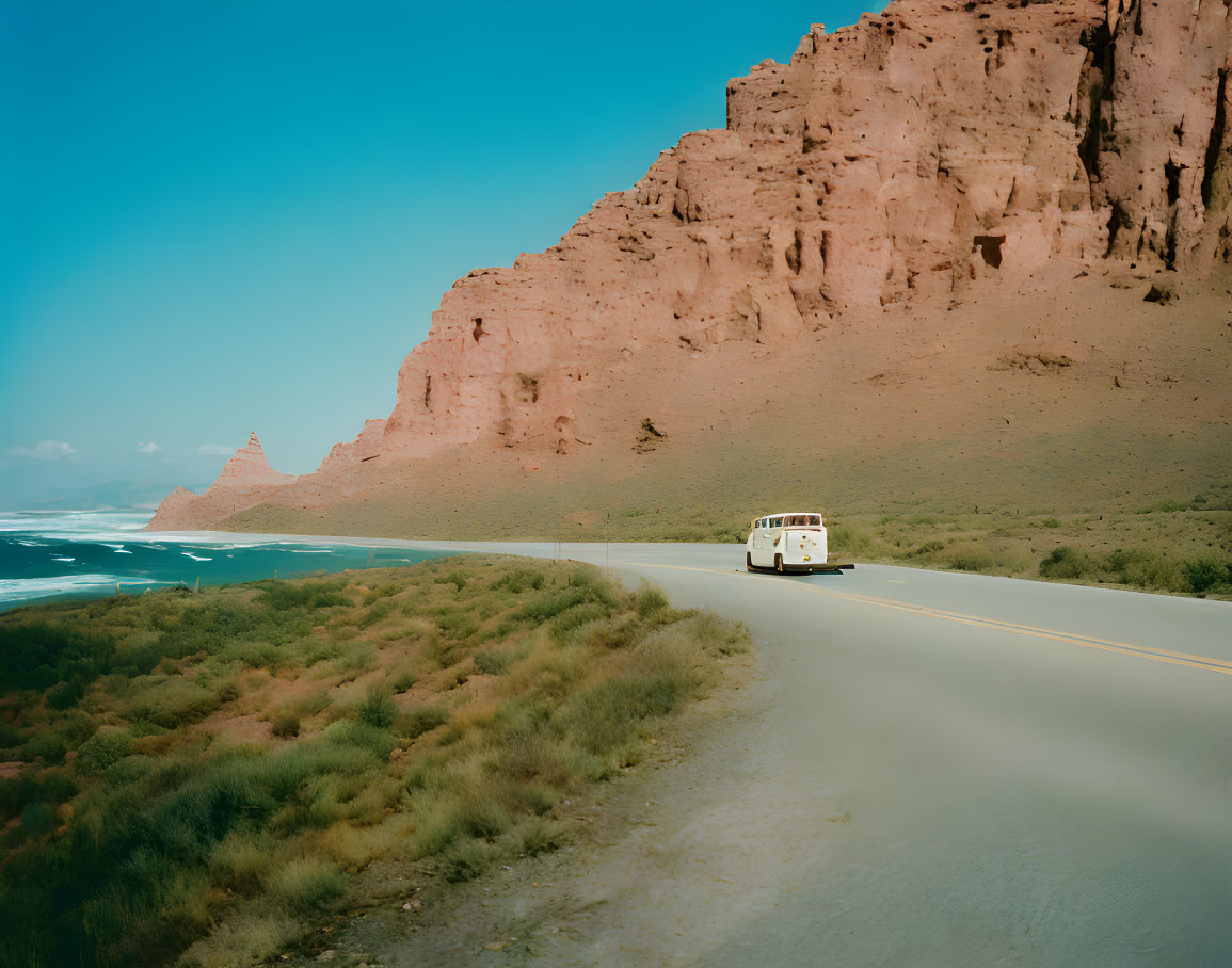 Vintage bus on coastal road with large rock formation and clear blue sky